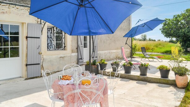An outdoor patio with a table set for two, covered by a blue umbrella, and surrounded by potted plants. - 3 bedroom awesome home in Razac-de-saussignac (razac-de-saussignac)