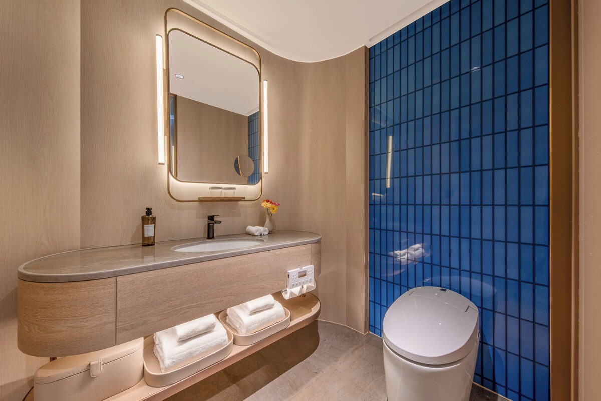 Un baño moderno con un tocador curvo, un espejo grande, un inodoro y paredes con azulejos azules.