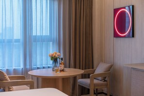 A hotel room with a round table, two chairs, a vase with flowers, a bottle, and a neon sign on the wall. - Crystal Orange Hotel Yancheng Municipal Government (Yancheng)