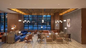 A modern hotel lobby with seating areas, large windows, and contemporary lighting fixtures.