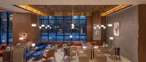 Un moderno vestíbulo de hotel con zonas de estar, ventanas amplias e iluminación contemporánea.
