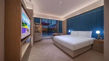Habitación de hotel moderna con una cama grande, un televisor sobre un soporte, un escritorio y vistas al exterior.
