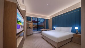 Habitación de hotel moderna con una cama grande, un televisor sobre un soporte, un escritorio y vistas al exterior.
