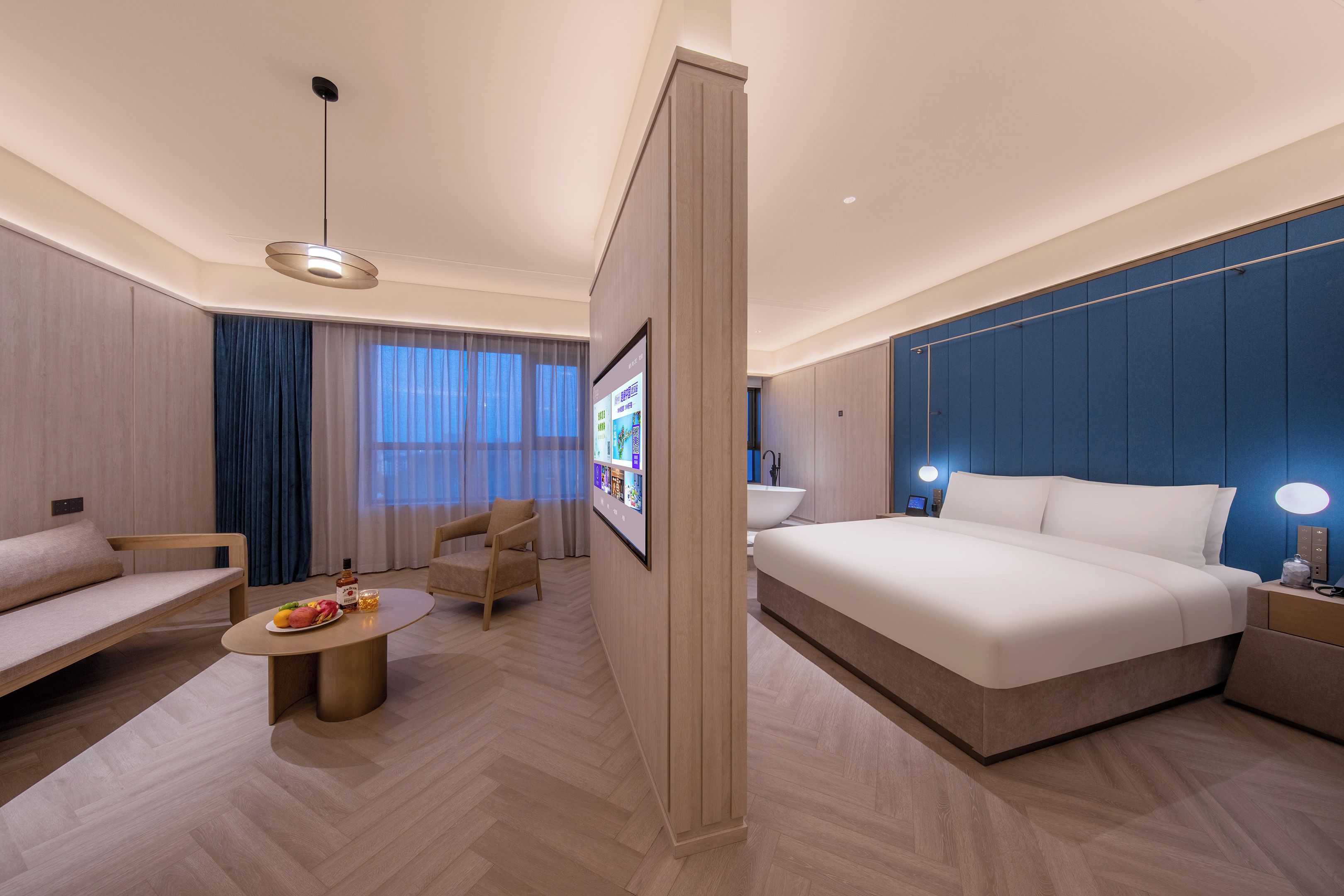 A modern hotel room with a large bed, a sofa, a coffee table, and a TV.