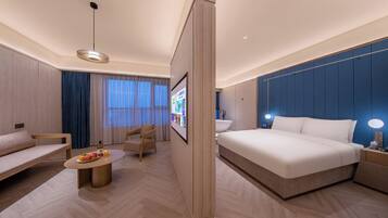 A modern hotel room with a large bed, a sofa, a coffee table, and a TV.