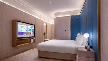 A modern hotel room with a large bed, a flat-screen TV mounted on the wall, and a bedside table with a lamp.