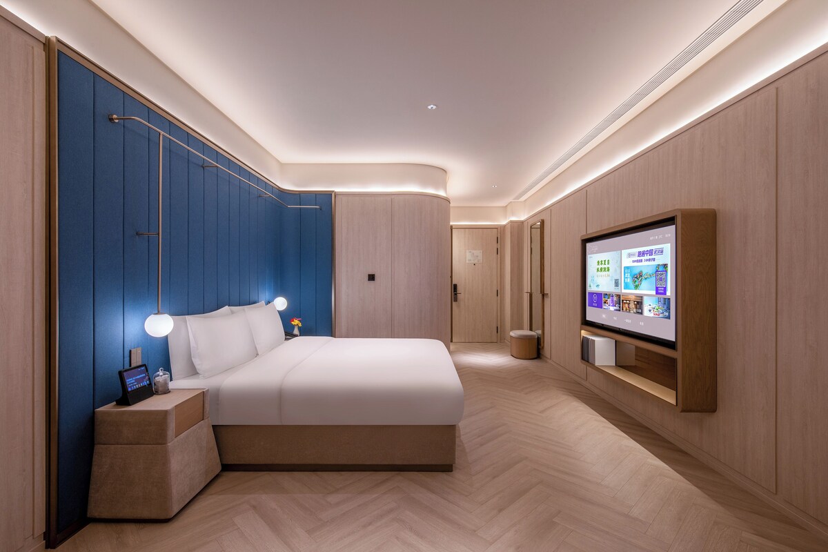 A modern bedroom with a large bed, bedside tables, a TV, and a wall-mounted shelf.