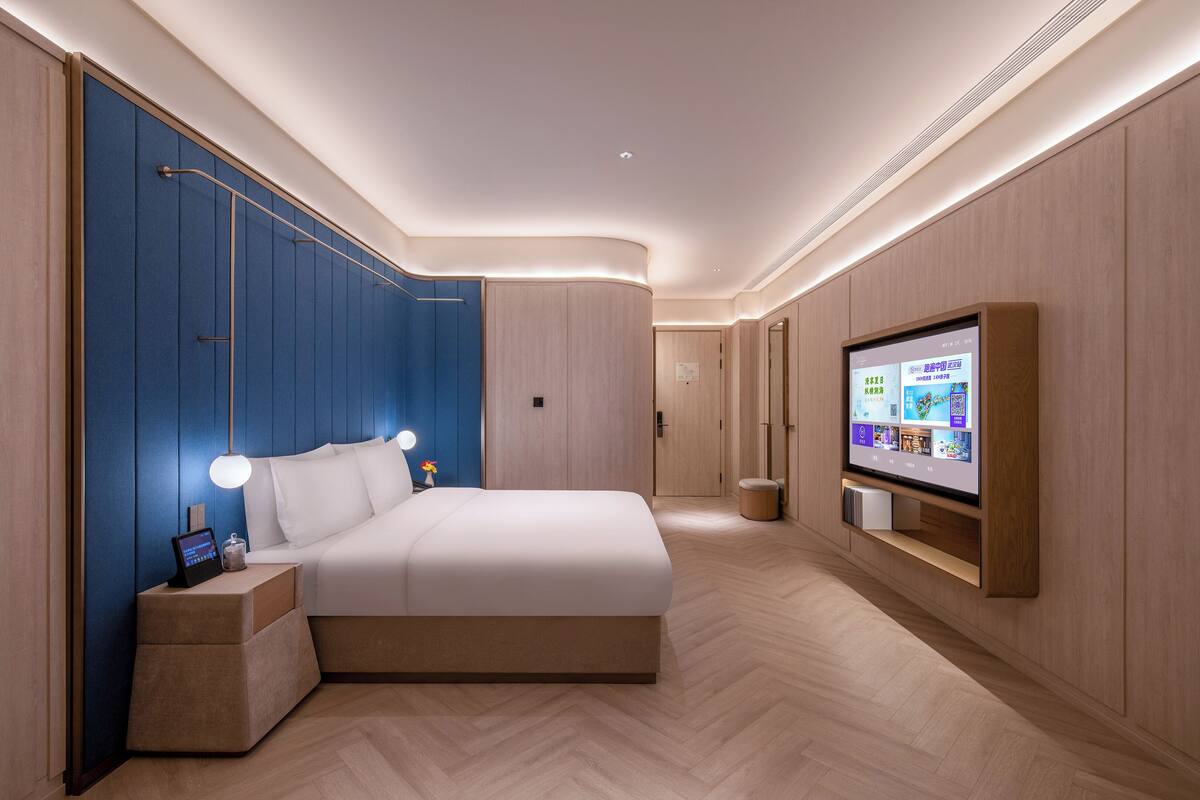 A modern bedroom with a large bed, bedside tables, a TV, and a wall-mounted shelf.