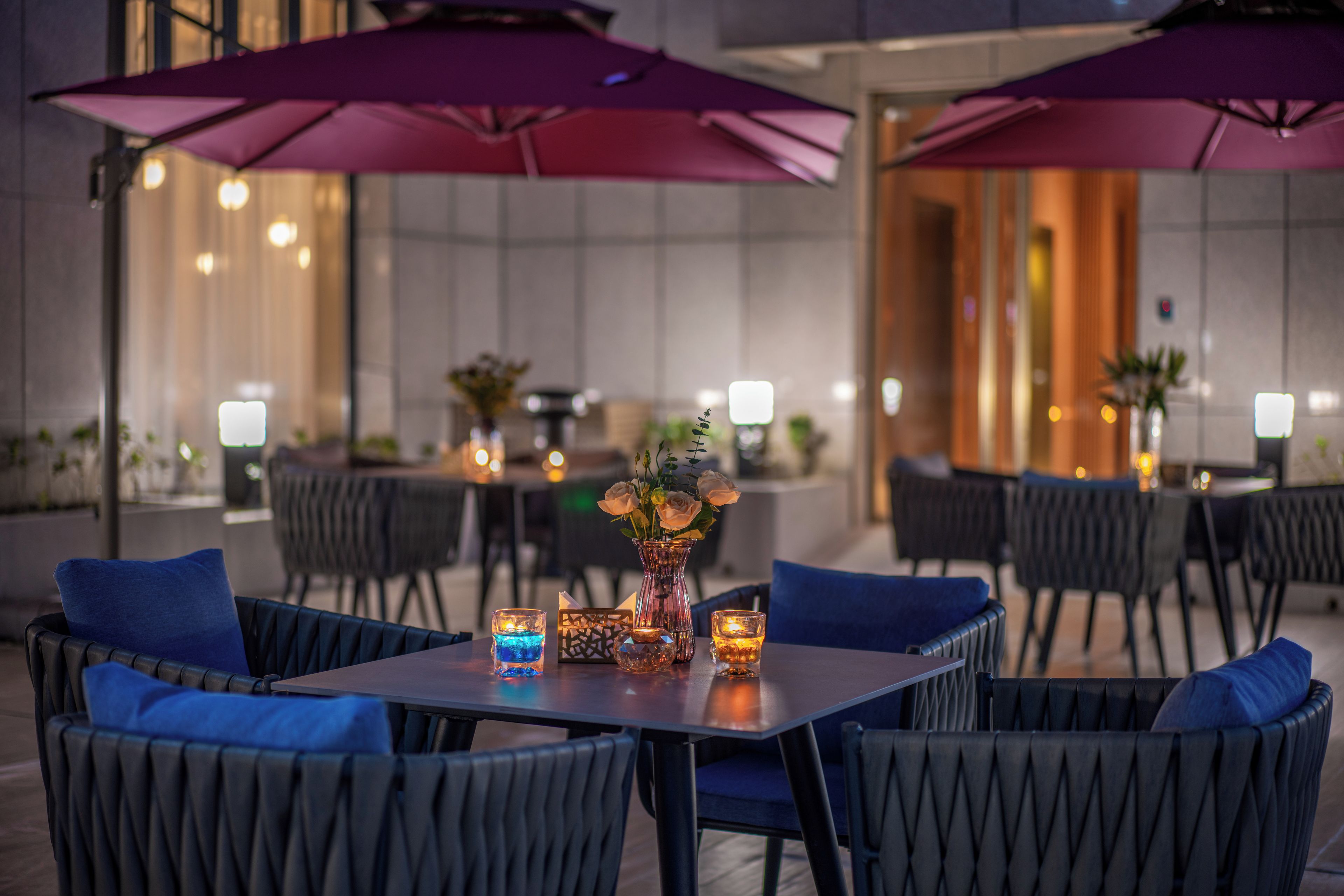 An outdoor dining area with tables and chairs, purple umbrellas, and candles.