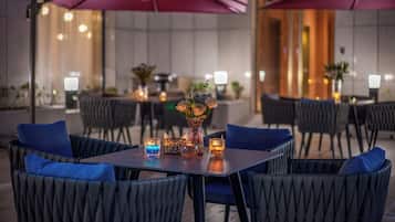 An outdoor dining area with tables and chairs, purple umbrellas, and candles.