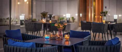 An outdoor dining area with tables and chairs, purple umbrellas, and candles.