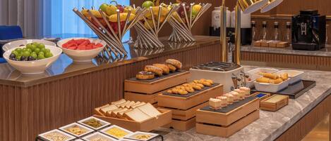 A buffet with various food items, including fruits, pastries, and beverages.