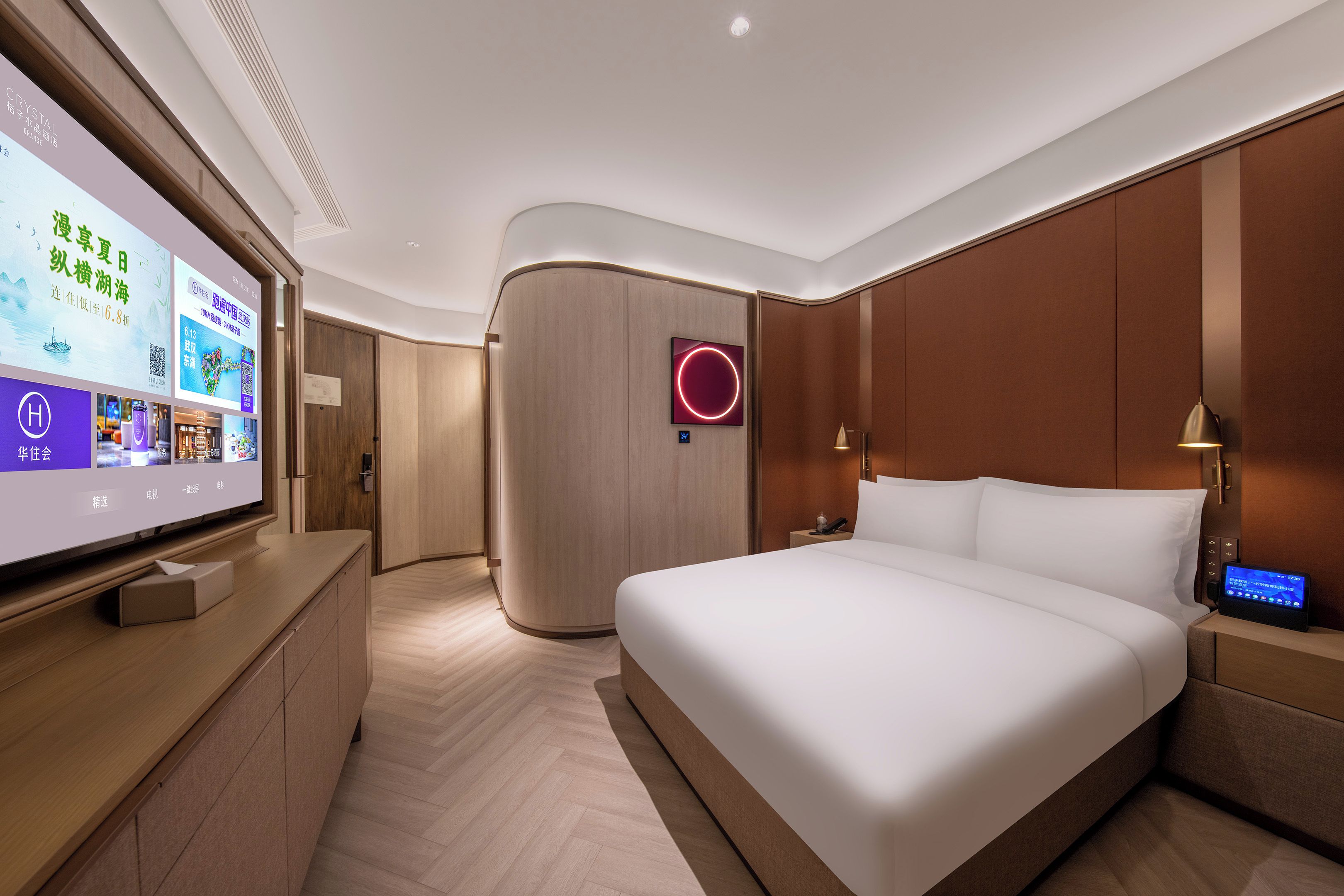Una habitación de hotel moderna con un televisor de pantalla plana grande, una cama con ropa blanca, un cabecero de madera y una mesita de noche con lámpara.