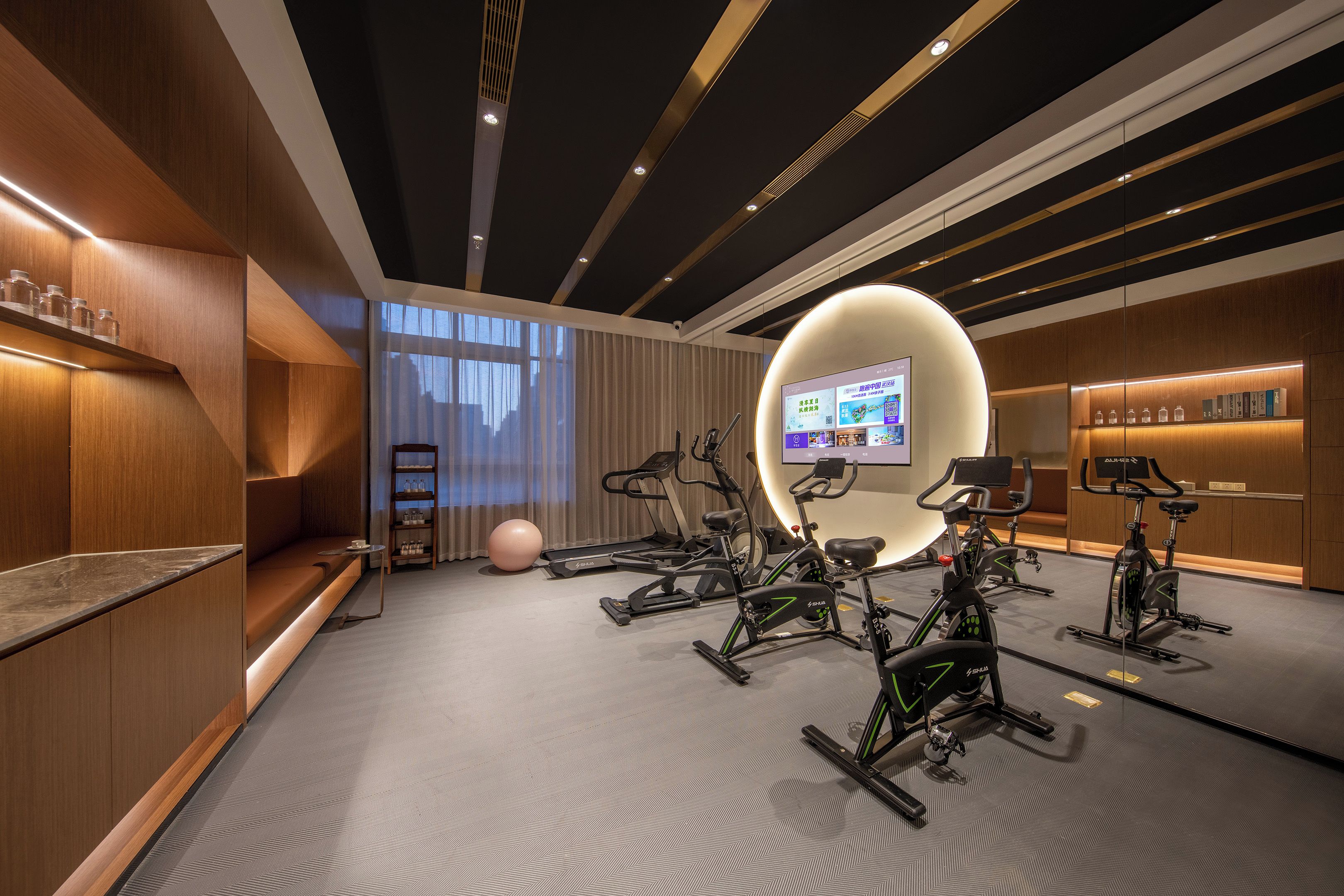 A modern fitness room with multiple stationary bikes, a large screen, and a well-lit space with wooden accents and a grey floor.