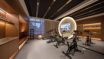 A modern fitness room with multiple stationary bikes, a large screen, and a well-lit space with wooden accents and a grey floor.
