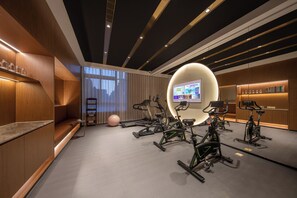 A modern fitness room with multiple stationary bikes, a large screen, and a well-lit space with wooden accents and a grey floor. - Crystal Orange Hotel Yancheng Municipal Government (Yancheng)