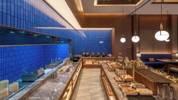 A modern buffet setup with a marble counter, blue tiled walls, and a seating area with a blue sofa.