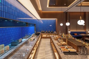 A modern buffet setup with a marble counter, blue tiled walls, and a seating area with a blue sofa. - Crystal Orange Hotel Yancheng Municipal Government (Yancheng)