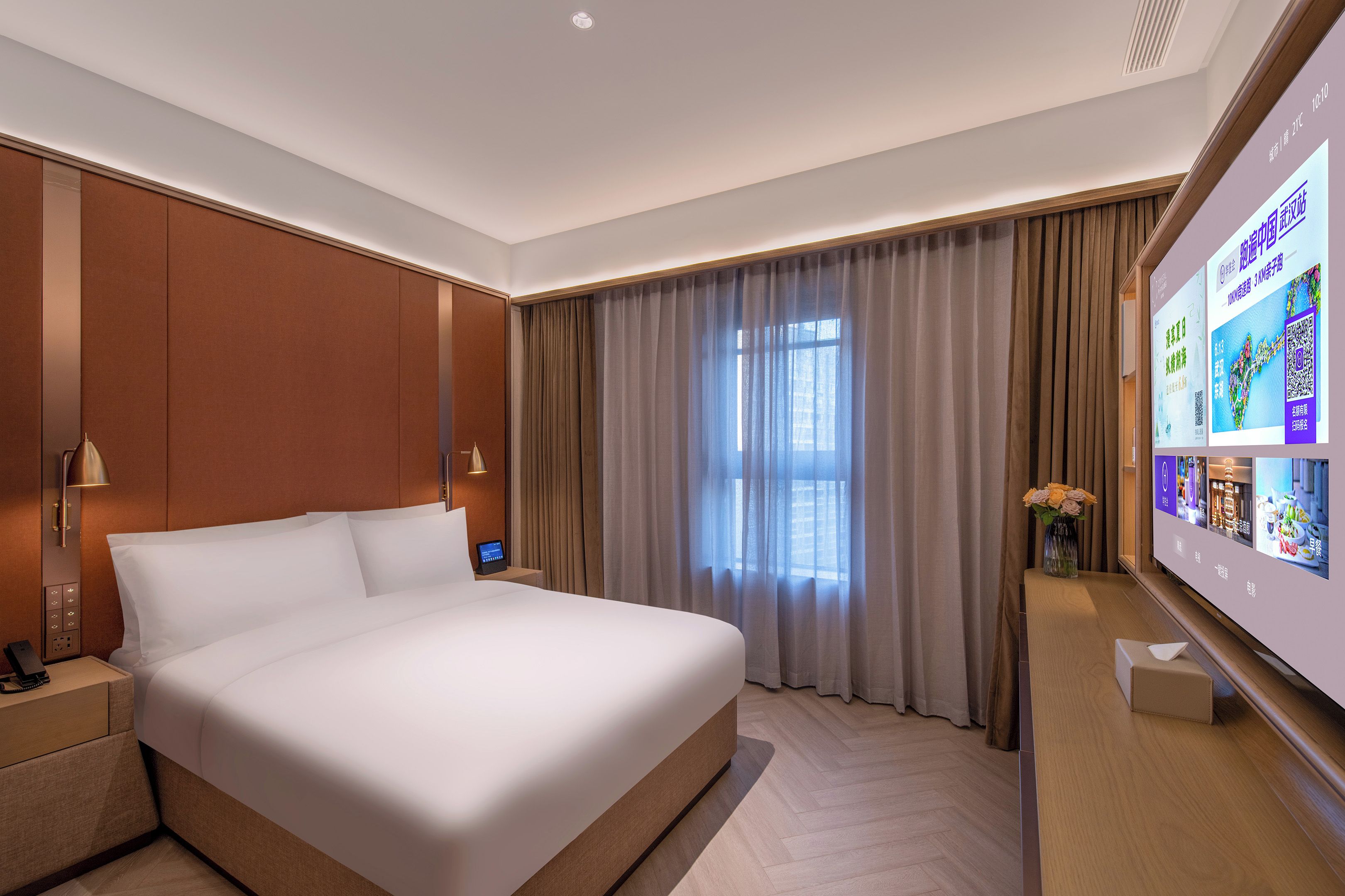 Una habitación de hotel moderna con una cama grande, una mesita de noche con lámpara, una pantalla de televisión y un ventanal con cortinas.