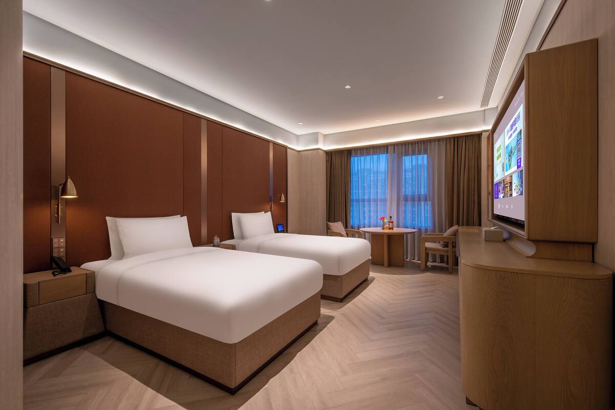 A hotel room with two beds, a desk, a chair, a TV, and a minibar.