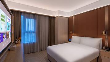 A hotel room with a large bed, a flat-screen TV, a bedside table with a lamp, and a window with curtains.