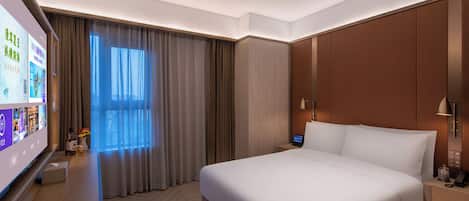 A hotel room with a large bed, a flat-screen TV, a bedside table with a lamp, and a window with curtains.