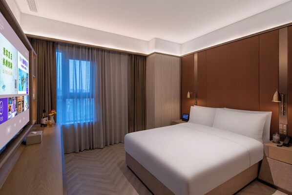 Habitación de hotel con una cama grande, un televisor de pantalla plana, una mesita de noche con lámpara y una ventana con cortinas.