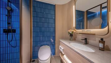 Un baño moderno con ducha de azulejos azules, inodoro blanco, lavabo con espejo y tocador de madera.
