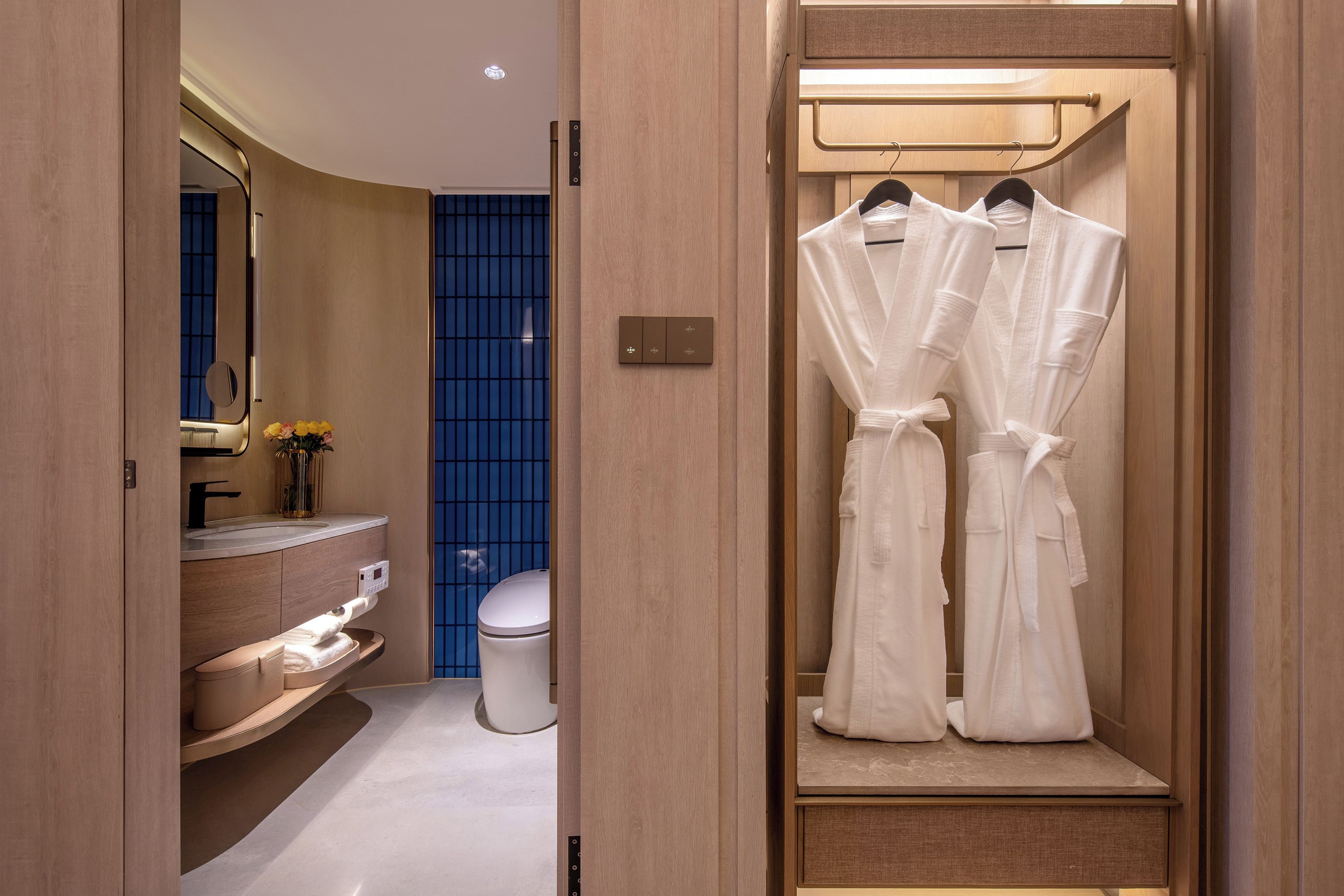 Une salle de bain moderne avec un meuble-lavabo en bois, des toilettes et un espace douche doté d’une porte en verre bleue.