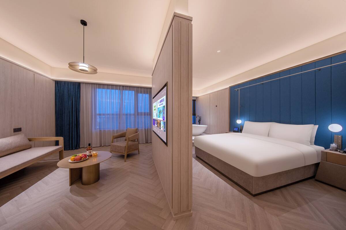 A modern hotel room with a large bed, a sofa, a coffee table, and a TV.