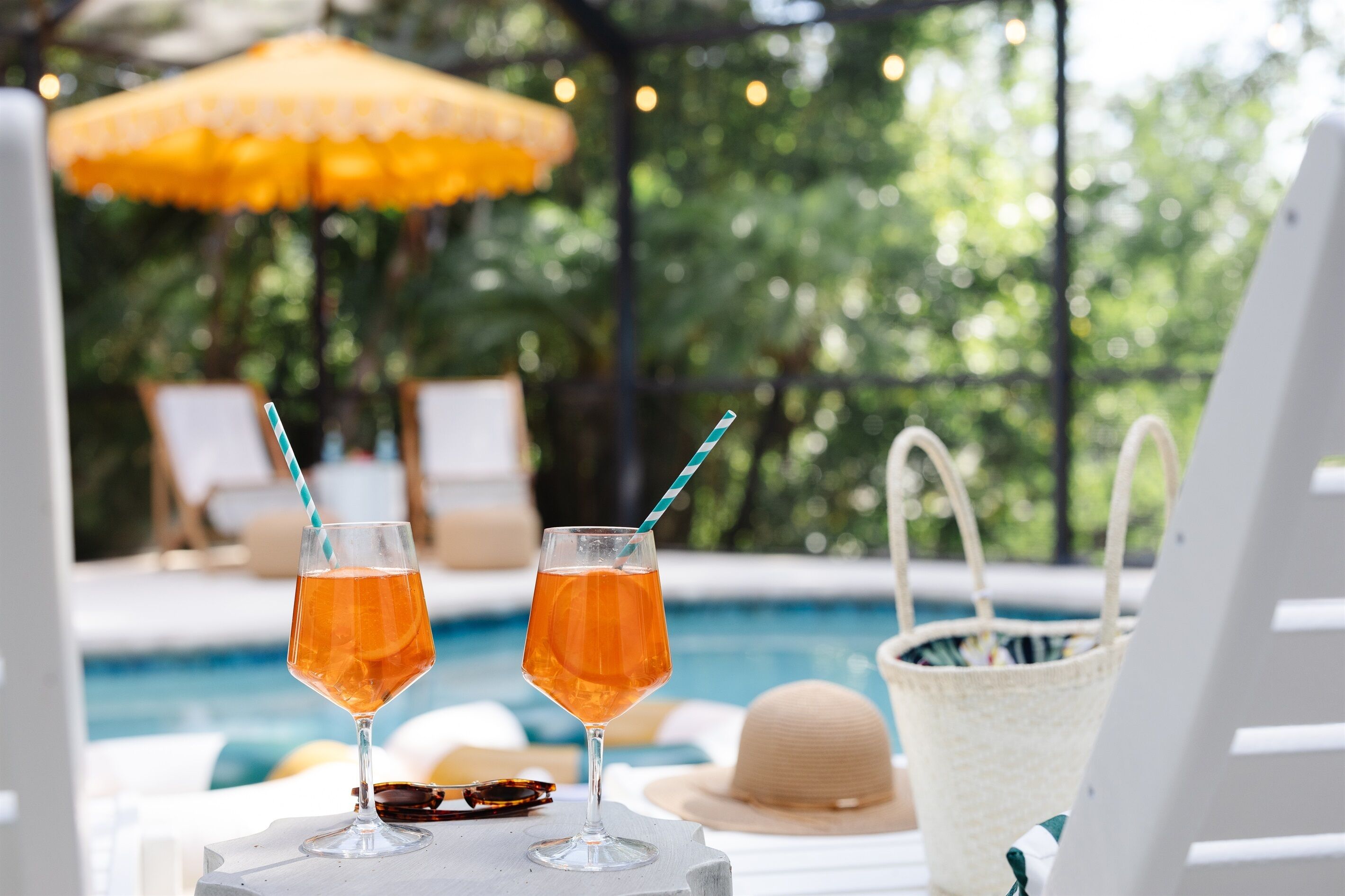 Deux cocktails sont posés sur une table près d’une piscine, à côté de chaises longues et d’un grand parasol.