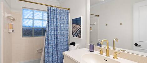A bathroom with a bathtub, a large mirror, a vanity with a sink and gold faucets, and a blue patterned shower curtain.
