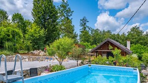 Une piscine bordée de pierres, entourée d’une végétation luxuriante et agrémentée d’un chalet en bois.