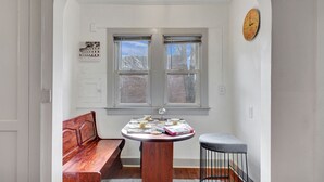A small room with a wooden bench, a round table with a clock, and two windows. - Cozy home with office walking distance to beach (Rochester)