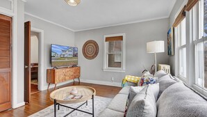 A living room with a television, a round wooden coffee table, a sofa, and a window with blinds. - Cozy home with office walking distance to beach (Rochester)