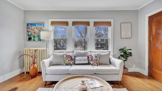 A living room with a sofa, a coffee table, a radiator, and a window with blinds. - Cozy home with office walking distance to beach (Rochester)