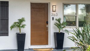 Une maison avec une porte en bois, le numéro « 363 » au-dessus, et deux plantes en pot de chaque cÎté.