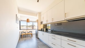 A modern kitchen with white cabinets, a black countertop, and a view through the window. - GuestReady - Apple beach hideaway with sea views (Colares)
