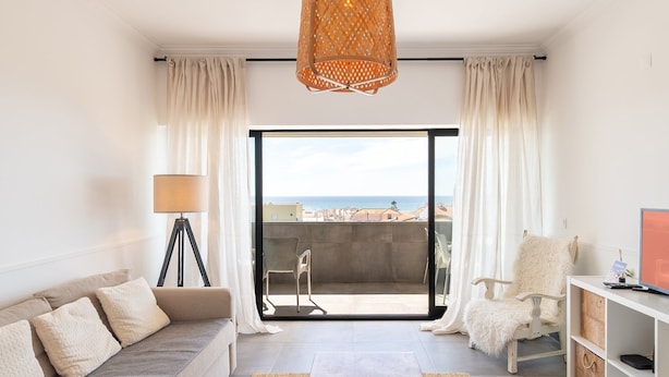A modern living room with a sofa, a chair, a lamp, and a view of the sea. - GuestReady - Apple beach hideaway with sea views (Colares)