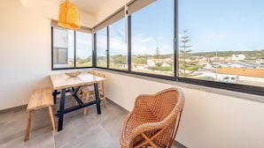 A room with a large window, a wooden table, a wicker chair, and a hanging light fixture. - GuestReady - Apple beach hideaway with sea views (Colares)