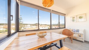 A modern room with a large window, a wooden table, a wicker chair, and a bookshelf. - GuestReady - Apple beach hideaway with sea views (Colares)