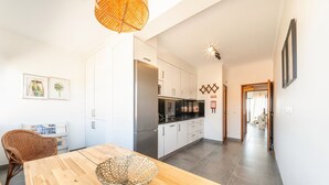A modern kitchen with white cabinets, a stainless steel refrigerator, and a wooden dining table with a decorative bowl. - GuestReady - Apple beach hideaway with sea views (Colares)