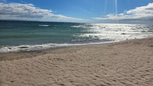 Ein Strand mit blauem Himmel und Sonnenlicht, das sich auf dem Wasser spiegelt.