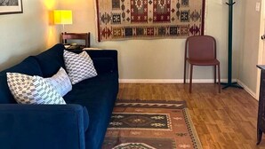 A living room with a dark blue sofa, patterned cushions, a decorative rug, a wall hanging, and a floor lamp. - The Starlight at Casa Hermosa, Gaze At Sleeping Lion Mountain From Your Porch! (Fort Davis)