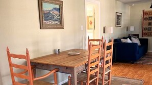 A dining area with a wooden table and chairs, a patterned rug, and a painting on the wall. - The Starlight at Casa Hermosa, Gaze At Sleeping Lion Mountain From Your Porch! (Fort Davis)