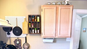 A compact kitchen with a stove, oven, and wooden cabinets. A pegboard with various kitchen items is mounted on the wall. - The Starlight at Casa Hermosa, Gaze At Sleeping Lion Mountain From Your Porch! (Fort Davis)
