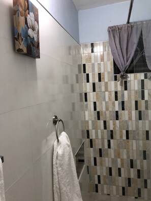 A bathroom with a tiled shower wall, a hanging shower curtain, and a towel rack with a towel. - Comfortable Stay  (Kingston)
