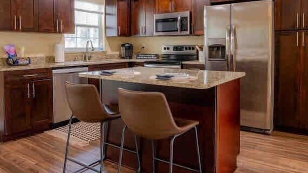 Una cocina con armarios de madera oscura, electrodomésticos de acero inoxidable y una isla central con dos taburetes de bar.
