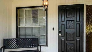 Un banco negro frente a una casa con una puerta negra y una ventana con persianas.