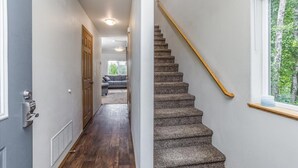 A hallway with a carpeted staircase, a door with a keypad lock, and a window with a view of trees. - Mountain View Haven - Luxe Townhouse with King Suite & Warm Garage (Wasilla)